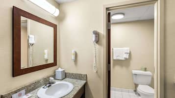 Un baño de hotel con lavamanos, espejo, secador de pelo y retrete.