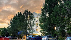 Un hotel con estacionamiento, árboles y un cielo al atardecer.