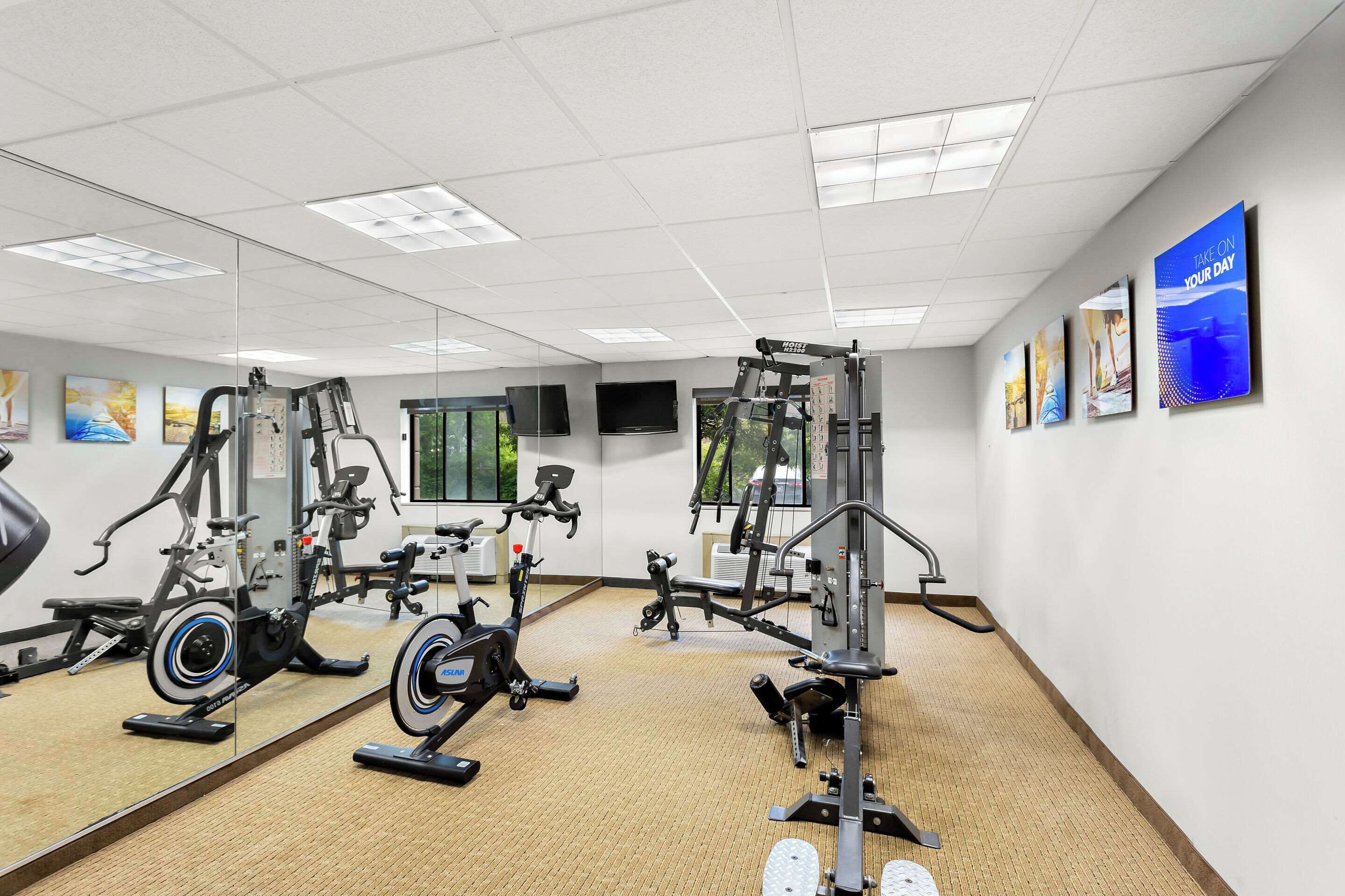 Een sportschool met diverse fitnessapparaten, grote spiegels en motiverende posters op de muren.
