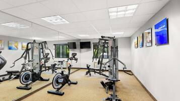 Een sportschool met diverse fitnessapparaten, grote spiegels en motiverende posters op de muren.