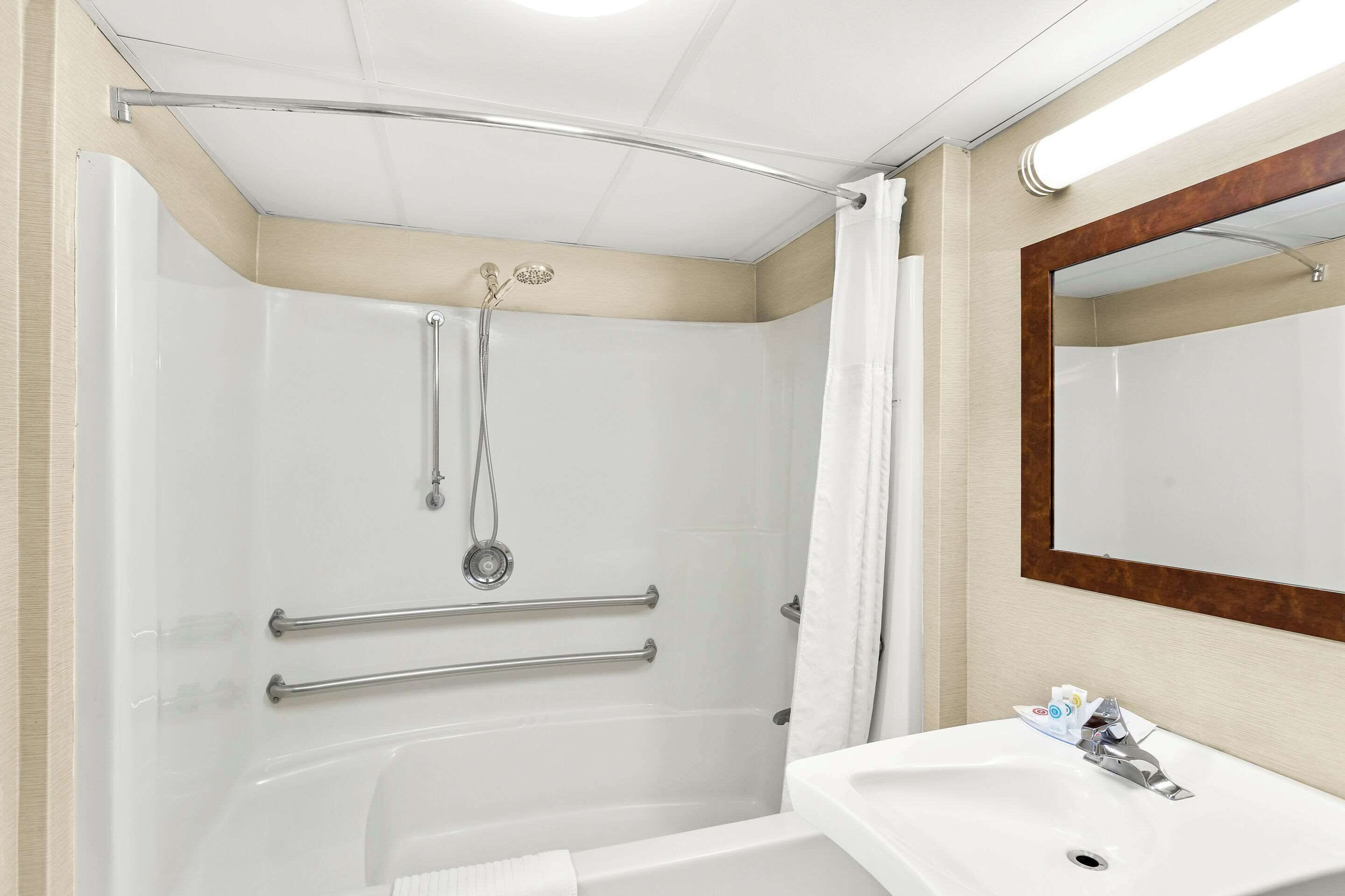 Un baño moderno con cabina de ducha a ras de suelo, barras de apoyo, lavamanos y espejo.