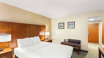A hotel room with a large bed, bedside table with a lamp, a small desk, a chair, and a door.