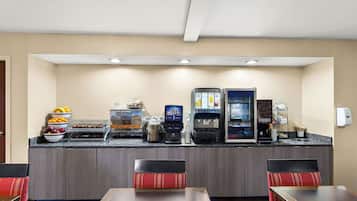 A hotel breakfast area with a self-service station, seating, and a counter with various food items.