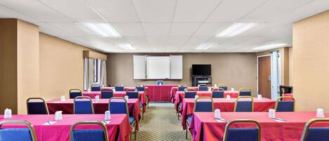 Un salón de conferencias con mesas y sillas, una pantalla de proyector y una televisión.