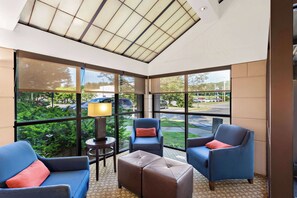 A sunroom with large windows, a sofa, two armchairs, a small table with a lamp, and a view of the parking lot. - Comfort Inn White River Junction (White River Junction)