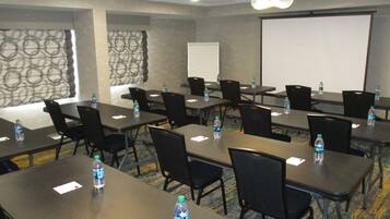 A conference room with tables, chairs, water bottles, a whiteboard, and a projector screen.