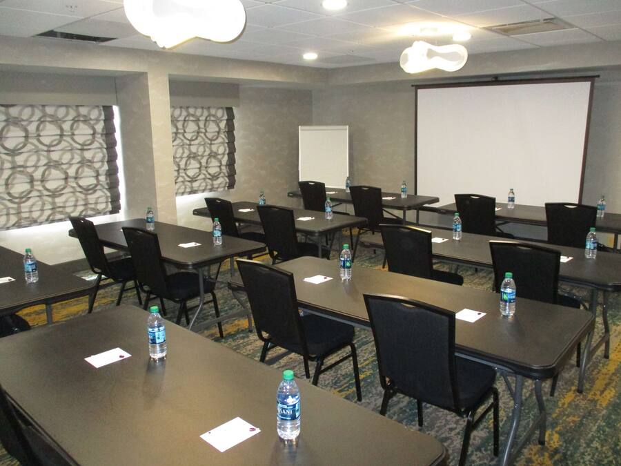 A conference room with tables, chairs, water bottles, a whiteboard, and a projector screen.