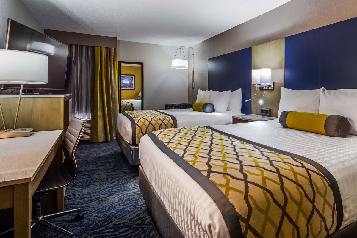 A hotel room with two beds, a desk, a chair, a TV, and a bathroom.