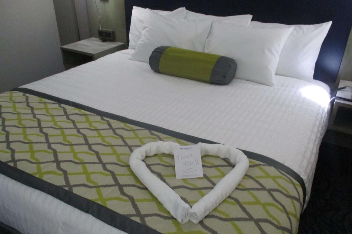 A neatly made bed with a heart-shaped towel and a thank you note on a hotel room.