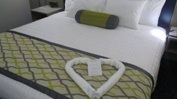 A neatly made bed with a heart-shaped towel and a thank you note on a hotel room.