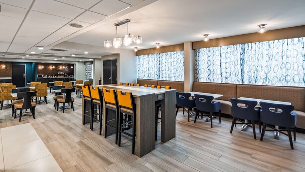 Um restaurante moderno com balcão central, áreas de estar e cozinha ao fundo.