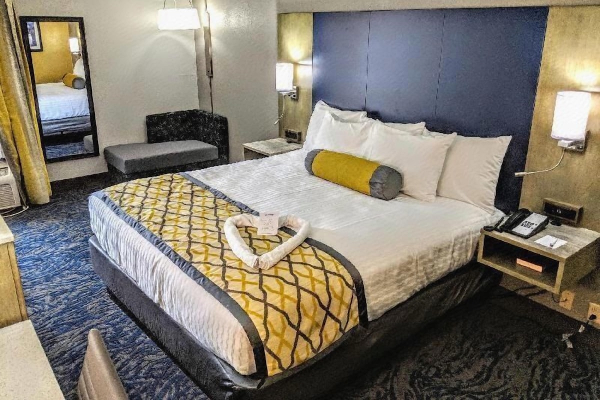 A hotel room with a large bed, bedside tables, a mirror, and a headboard.