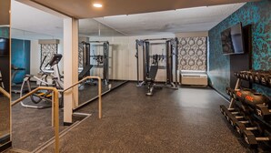 Uma academia com equipamentos de ginástica, um espelho na parede e uma televisão.