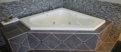 A modern bathroom with a freestanding bathtub, dark patterned tiles, and a small shelf with toiletries.