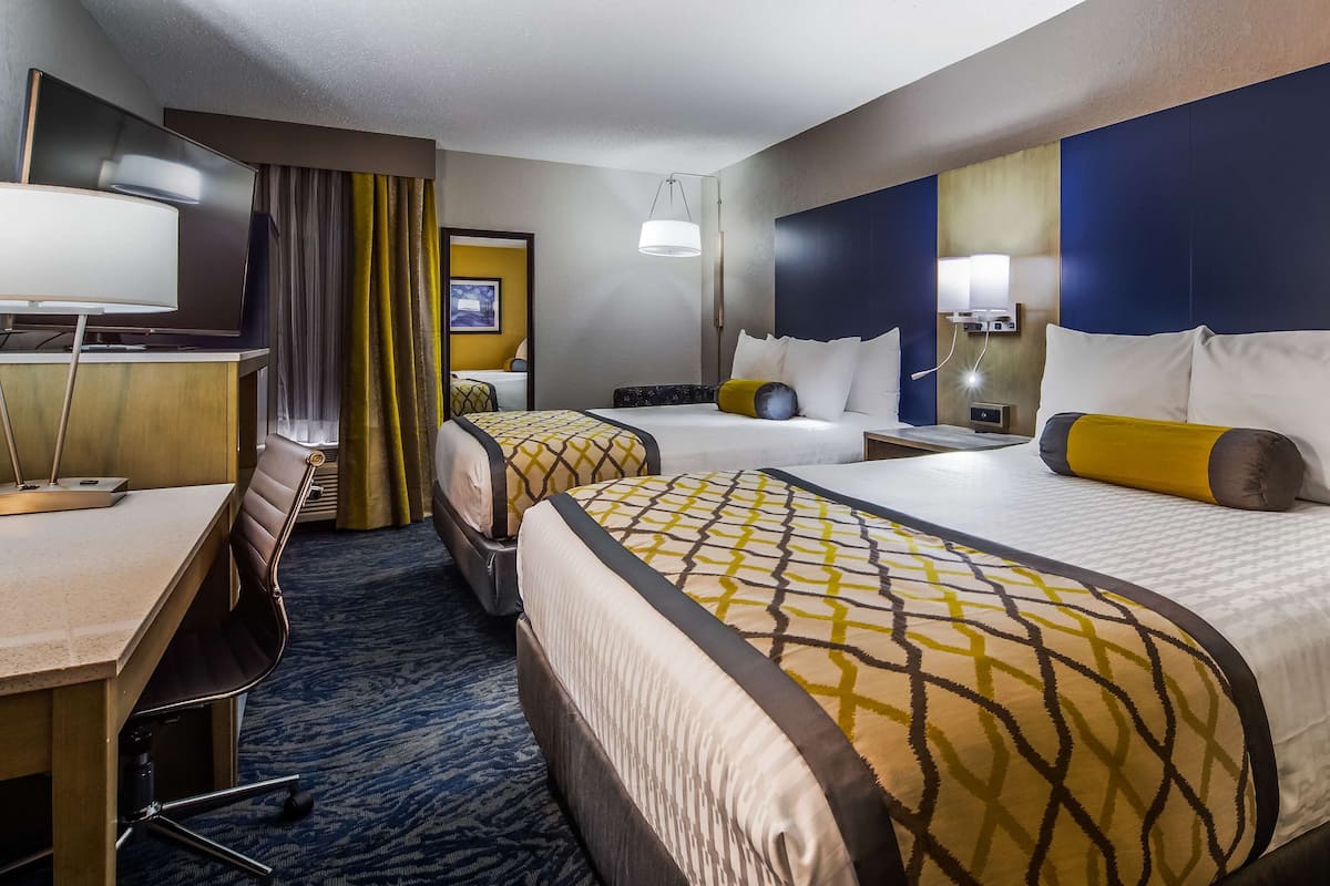 A hotel room with two beds, a desk, and a chair.