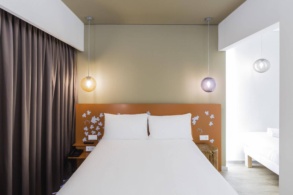 A modern hotel room with a large bed, two pendant lights, a nightstand, and a wooden nightstand with a lamp.