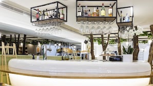 A modern bar area with a central island, bar stools, hanging wine glasses, and shelves with bottles.
