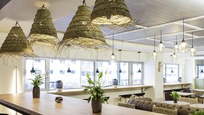 A modern interior with a long wooden bar, black bar stools, and hanging woven light fixtures.