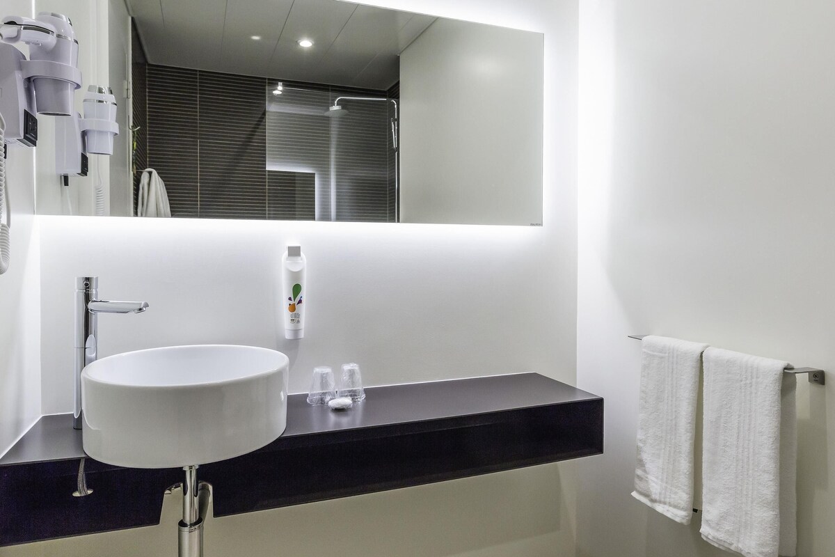 A modern bathroom with a large mirror, a white sink, a black countertop, and a towel rack.