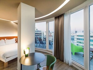 Enjoy city views from the large window in this stylish room with a round table, comfortable chair, and plush bed.