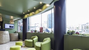 A modern waiting area with green seating, a large window with a city view, and a reception desk with a computer monitor.
