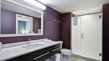 A modern bathroom with a dual sink vanity, a large mirror, a toilet, and a walk-in shower.