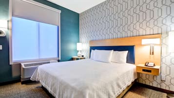 Habitación de hotel con una cama grande, una mesita de noche con lámpara, teléfono y ventana con persianas.