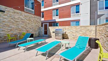 A rooftop patio with lounge chairs, a grill, and a stone wall.