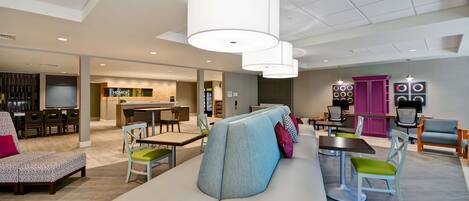 Ein moderner Lounge-Bereich mit einer Couch, Sesseln, Tischen und einer Küche im Hintergrund.