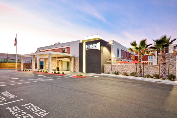 Un hotel moderno con un llamativo letrero que dice 'HOME', un acceso cubierto y un estacionamiento con flechas direccionales.