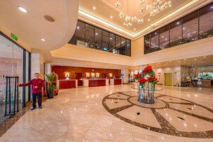 A spacious lobby with a reception desk, a large decorative fountain, and a high ceiling with chandeliers.