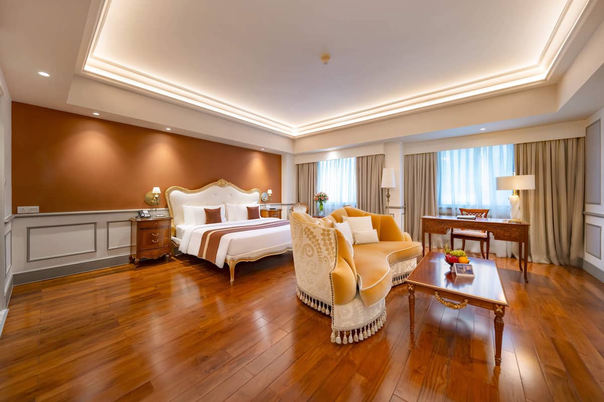 A spacious hotel room with a large bed, a sofa, a desk, and a view of the city.