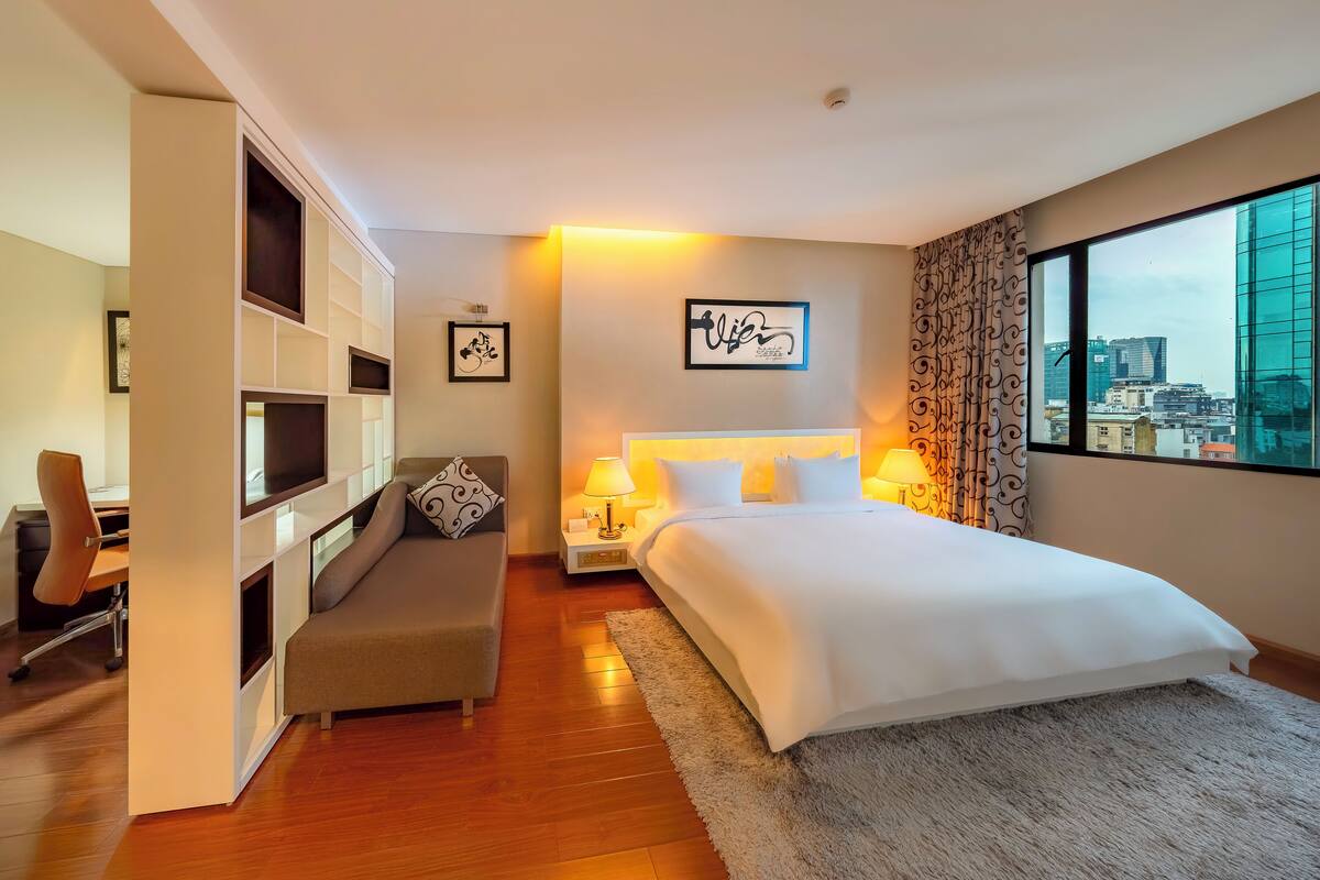 A modern hotel room with a large bed, a desk, and a seating area.