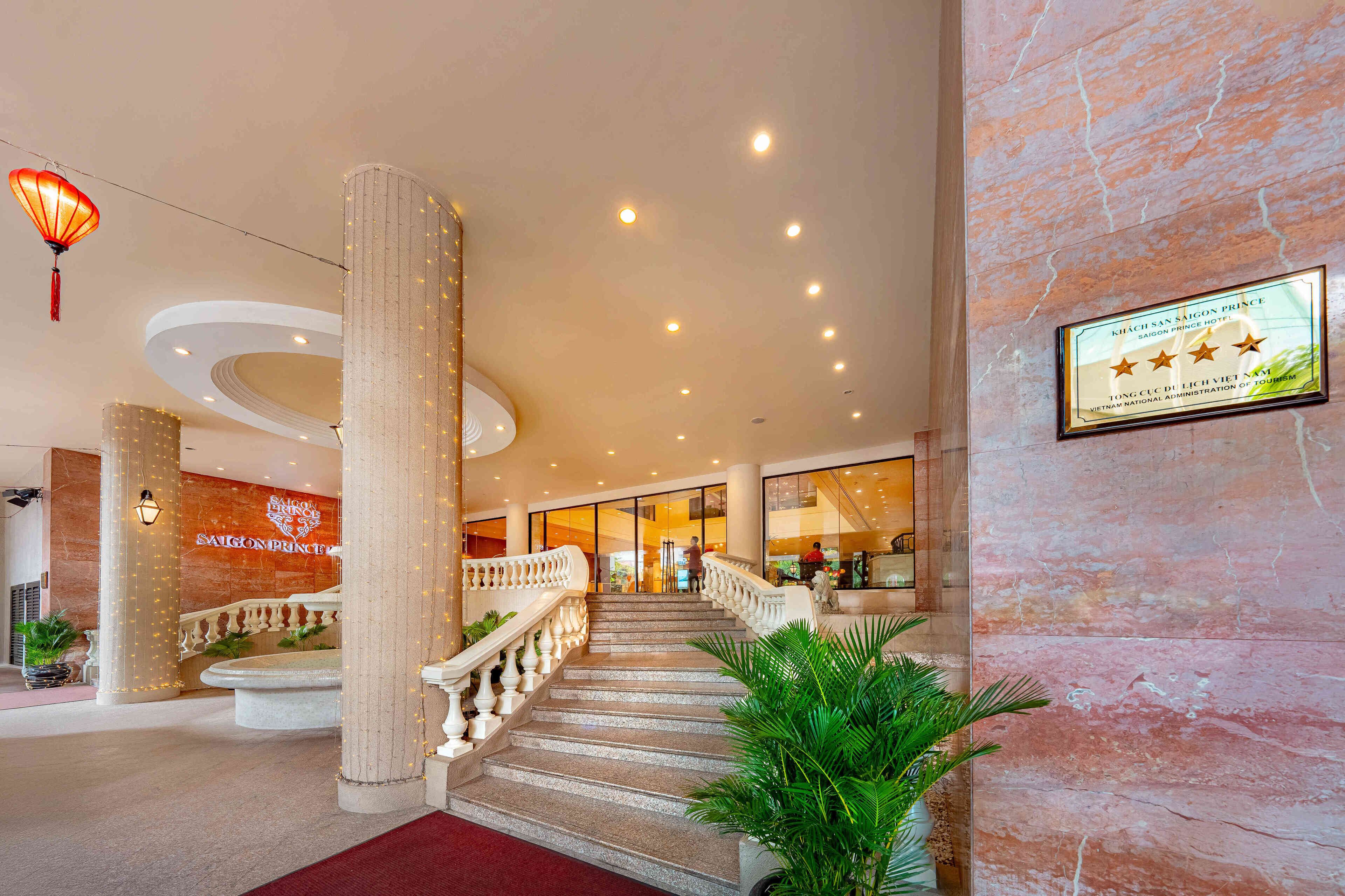 A hotel lobby with a marble reception desk, a staircase with a balustrade, and a sign on the wall.