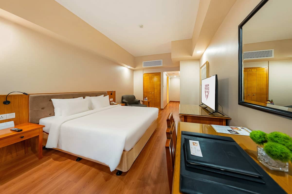 A hotel room with a large bed, wooden floor, a desk with a mirror, and a television.