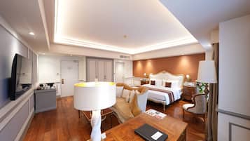 Una habitación de hotel con piso de madera, una cama con cabecera, una mesita de noche, una lámpara, una silla, un escritorio con lámpara y un televisor.
