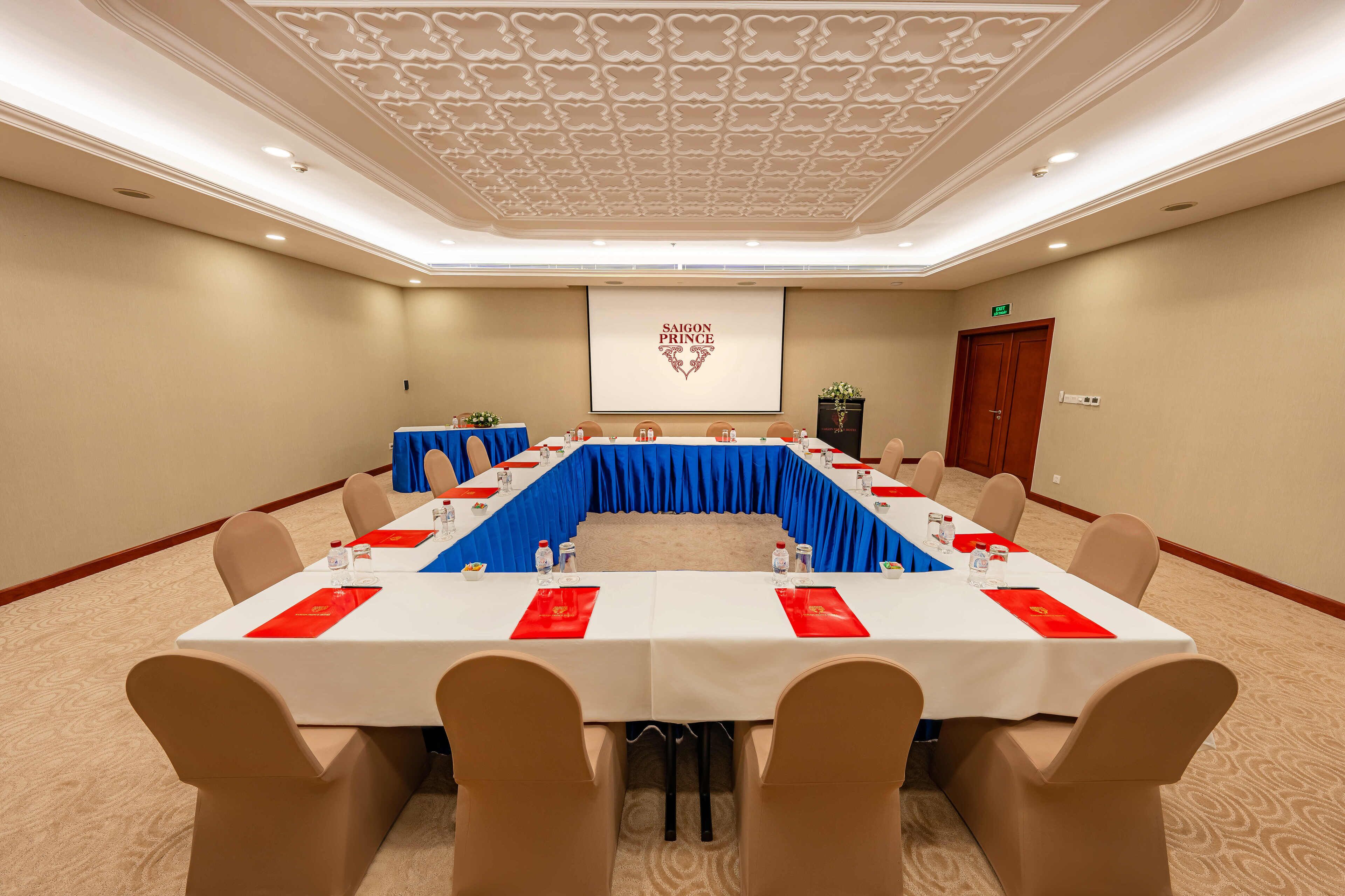 A conference room with a long table, beige chairs, and a projector screen displaying "SAIGON PRINCE".