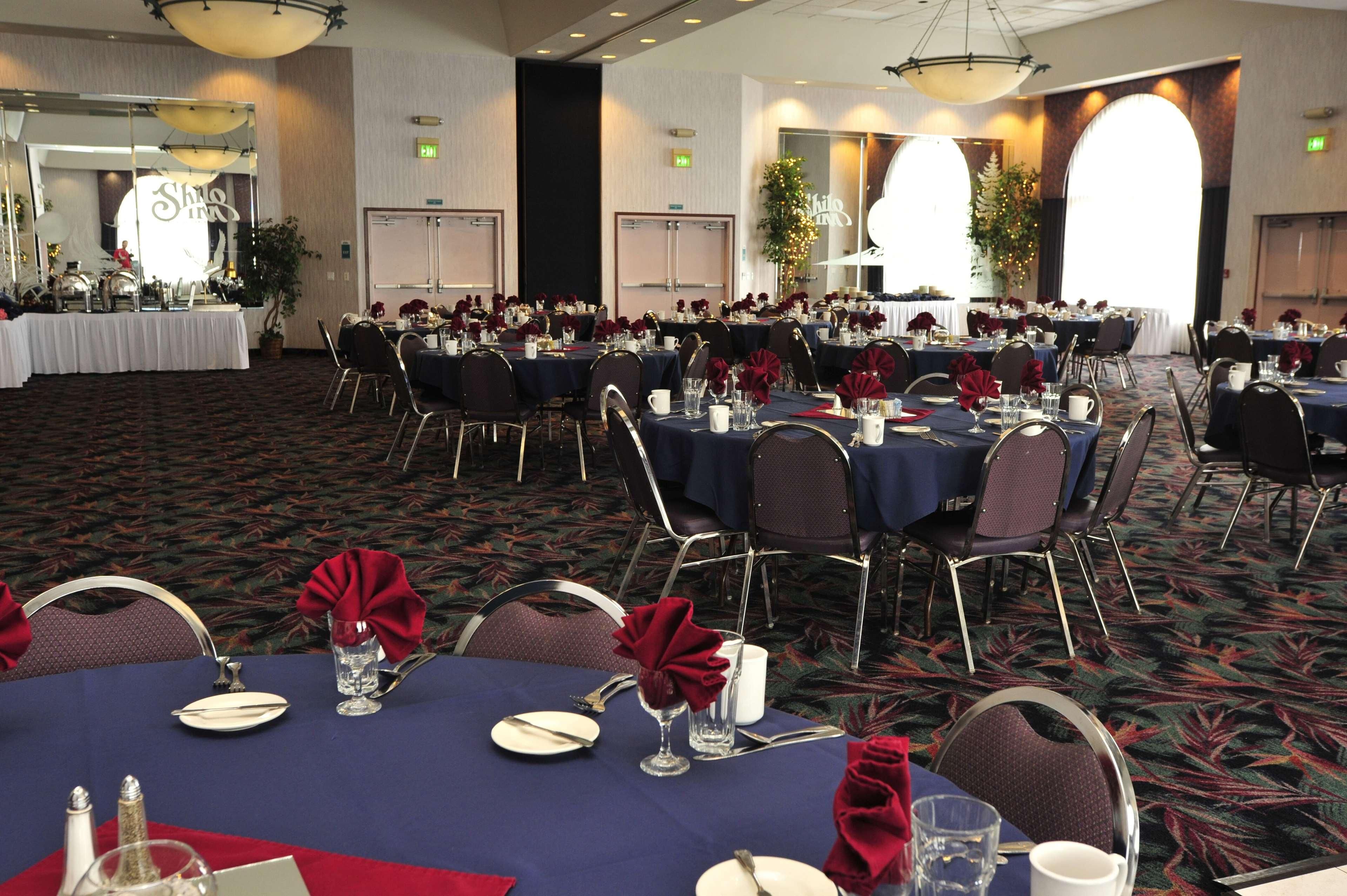 A banquet hall with round tables set for dining, featuring dark tablecloths and red napkins.