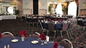 A banquet hall with round tables set for dining, featuring dark tablecloths and red napkins.