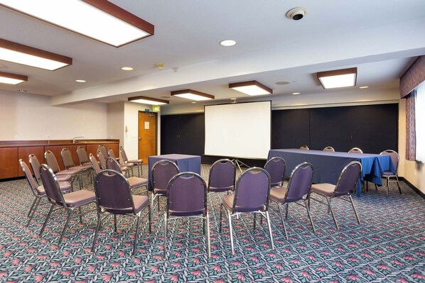 A conference room with a long table, chairs, a projector screen, and a carpeted floor.