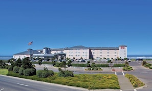 A large hotel with multiple floors, a parking lot, and a flagpole with an American flag. - Shilo Inn Suites Ocean Shores (Ocean Shores)