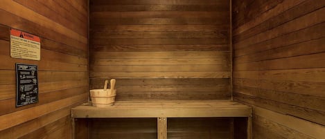 Una sauna con paredes de madera y un banco. Hay un cartel de advertencia en la pared y un cubo pequeño en el banco.