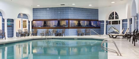 Une piscine intérieure avec un mur carrelé et de nombreuses fenêtres permettant d’admirer le paysage.