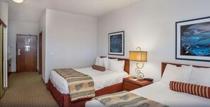 A hotel room with two beds, a nightstand with a lamp, and a door.