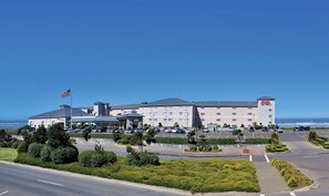 A large hotel with multiple floors, a parking lot, and a flagpole with an American flag. - Shilo Inn Suites Ocean Shores (Ocean Shores)