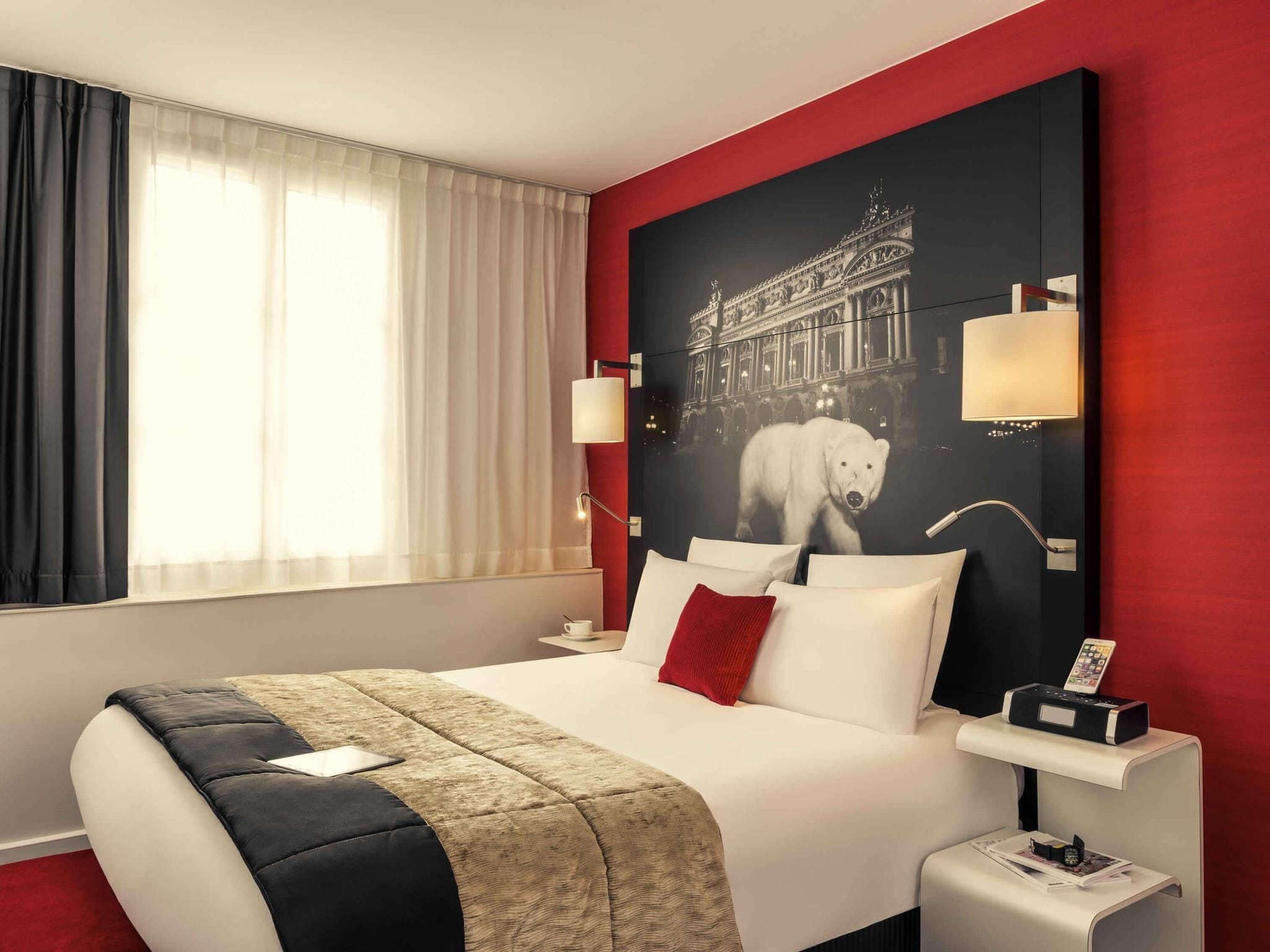 A hotel room with a large bed, a red accent wall, a polar bear image, and a nightstand with a lamp.