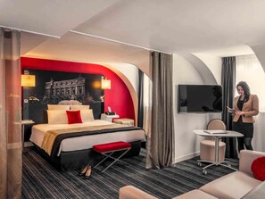A hotel room with a bed, a desk, a TV, and a view of a building. - Mercure Paris Opéra Louvre (Paris)