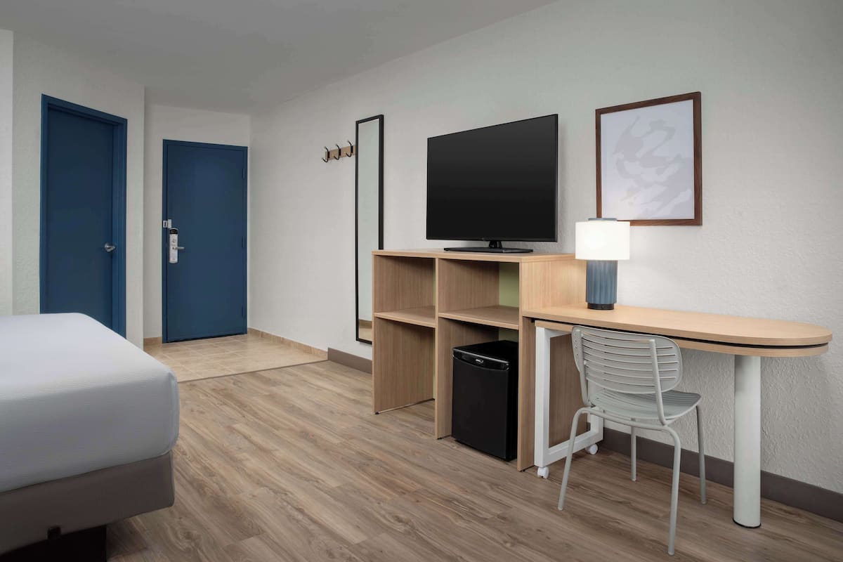 Una habitación de hotel con una cama, un escritorio con televisor, una silla y un cubo de basura.