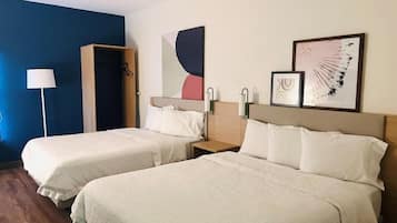 Quarto de hotel com duas camas, mesa de cabeceira, luminária e arte na parede.