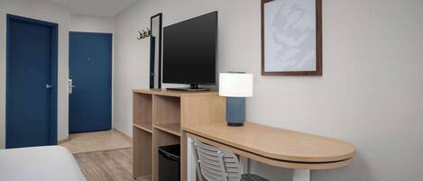Habitación de hotel con cama, escritorio con silla, televisor y un cuadro en la pared.